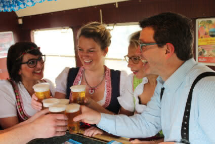 Gruppe in Tracht stößt mit Bier an im Partyzug auf dem Weg nach Cannstatt