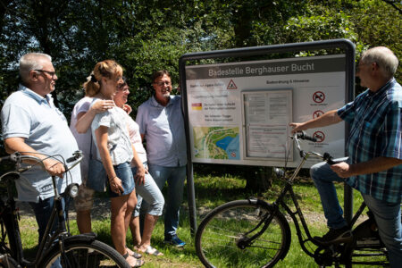 Gruppe schaut sich auf einer Fahrradtour am Hennesee gemeinsam eine Infotafel an