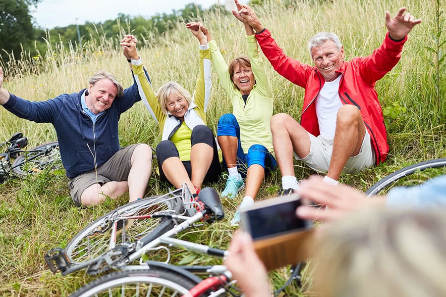 Vier Senioren sitzen im Gras in dem auch ihre Fahrräder liegen und jemand macht davon ein Foto mit einem Handy